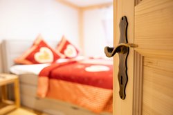  Zimmer-Bergzauber, Komfortables Schlafzimmer mit roten Bettbezügen, großen Kissen und Panoramafenster.