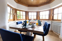 Helles Esszimmer mit gedecktem Holztisch und blauen Stühlen in einer Ferienwohnung.