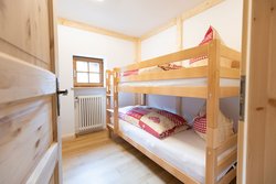 GipfelHimmel, gemütliches Schlafzimmer mit stabilem Etagenbett und Holzdekor. Einladendes Schlafzimmer mit einem massiven Holzetagenbett. Die Fenster mit Holzrahmen und der helle Holzfußboden unterstreichen das gemütliche Ambiente. 